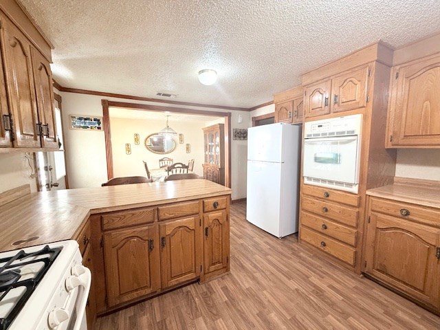 kitchen featuring light wood-type flooring, ornamental molding, white appliances, a peninsula, and light countertops