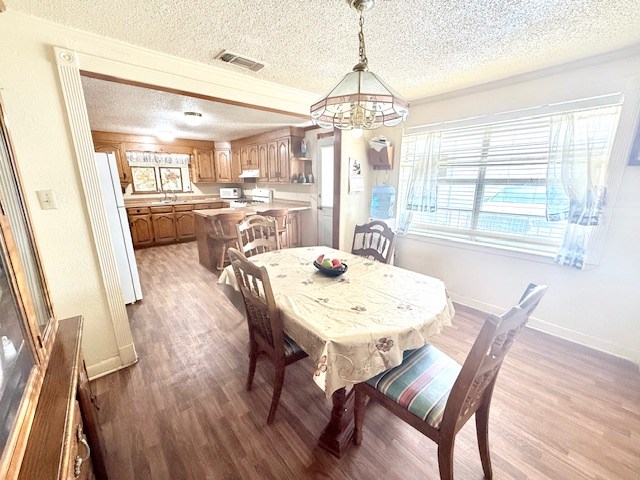 dining room with a textured ceiling, wood finished floors, visible vents, and baseboards