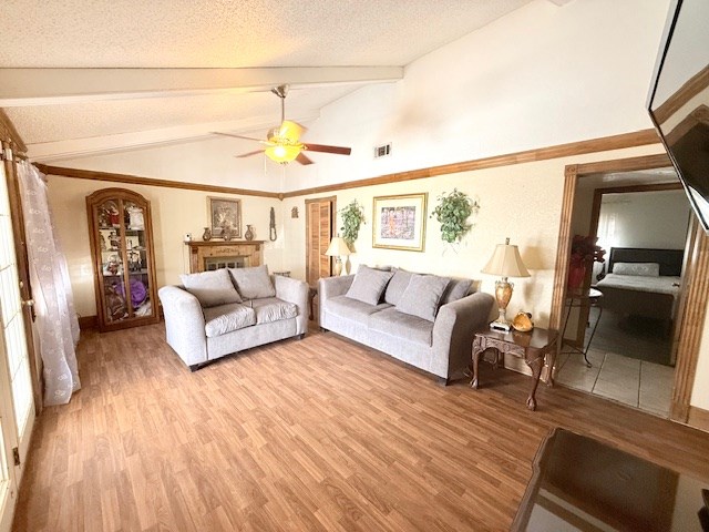 living room with a ceiling fan, visible vents, lofted ceiling with beams, light wood-style floors, and a textured ceiling