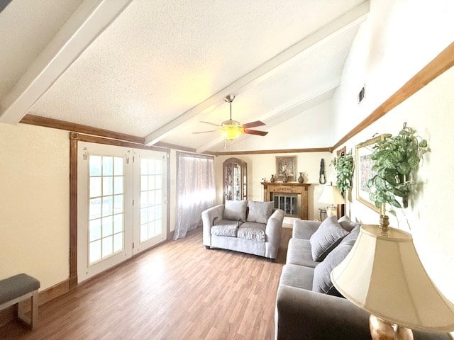 living room featuring ceiling fan, lofted ceiling with beams, light wood-style flooring, a glass covered fireplace, and a textured ceiling