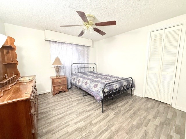 bedroom with baseboards, ceiling fan, light wood-style flooring, a closet, and a textured ceiling