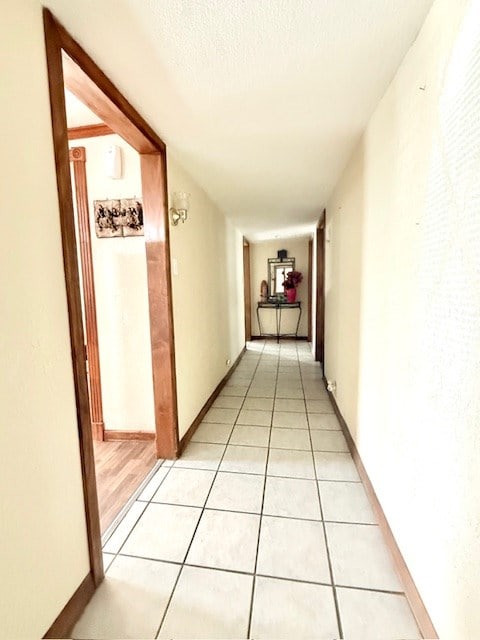 corridor featuring light tile patterned flooring, baseboards, and a textured ceiling