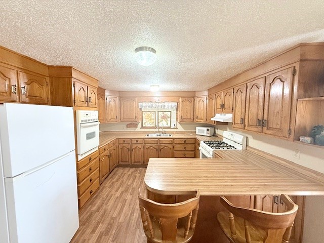 kitchen with white appliances, a peninsula, a sink, light countertops, and under cabinet range hood