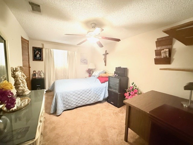 bedroom with light carpet, visible vents, a textured ceiling, and a ceiling fan