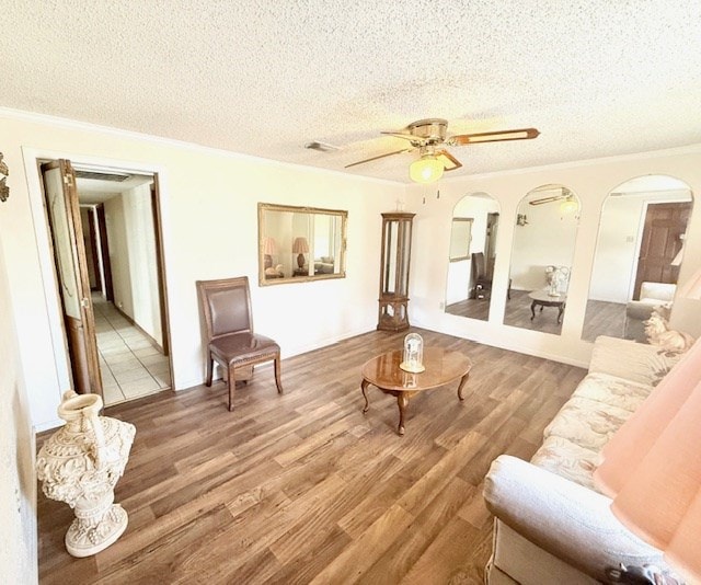 living area featuring a ceiling fan, wood finished floors, arched walkways, a textured ceiling, and crown molding