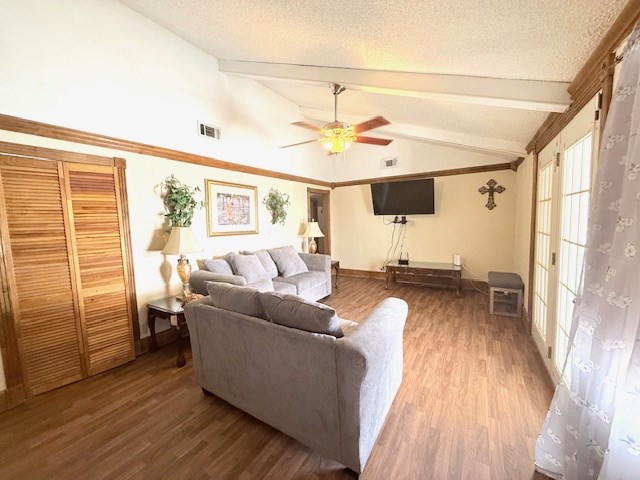 living room with wood finished floors, visible vents, vaulted ceiling with beams, ceiling fan, and a textured ceiling