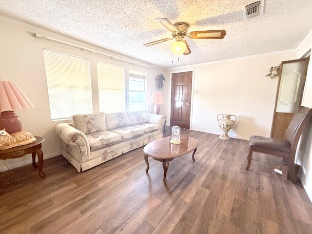 living room featuring visible vents, ornamental molding, a textured ceiling, and wood finished floors