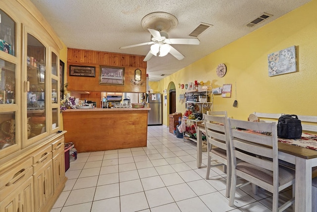 kitchen with kitchen peninsula, a textured ceiling, ceiling fan, light tile patterned floors, and stainless steel refrigerator