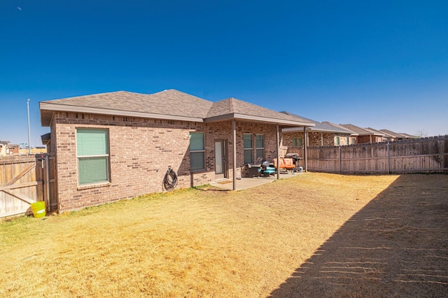 rear view of property with a yard, a patio, brick siding, and a fenced backyard