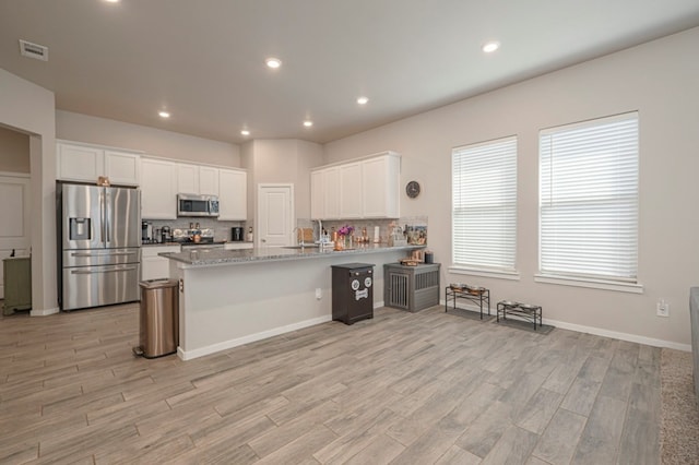 kitchen featuring light wood-style flooring, stainless steel appliances, a peninsula, white cabinets, and decorative backsplash