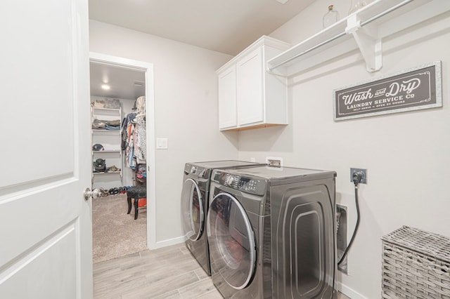 laundry room featuring baseboards, cabinet space, light wood-style flooring, and washer and clothes dryer