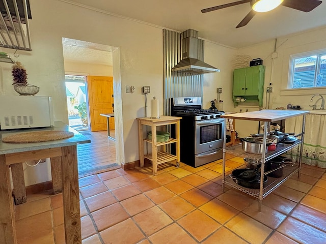 kitchen featuring wall chimney range hood, green cabinetry, gas range, ceiling fan, and light tile patterned floors