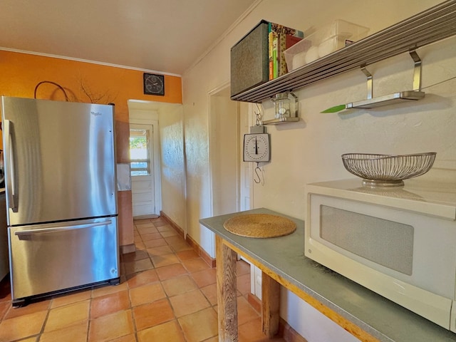 kitchen featuring stainless steel fridge, light tile patterned flooring, and ornamental molding