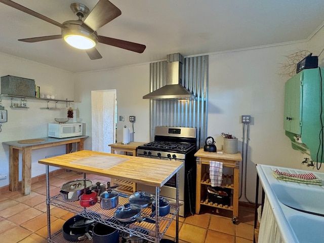 kitchen with stainless steel gas range oven, wall chimney exhaust hood, light tile patterned floors, and green cabinetry