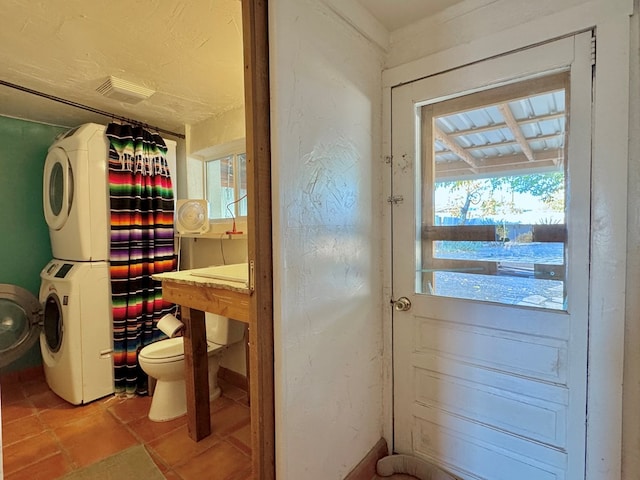 bathroom featuring tile patterned floors, toilet, plenty of natural light, and stacked washer and clothes dryer