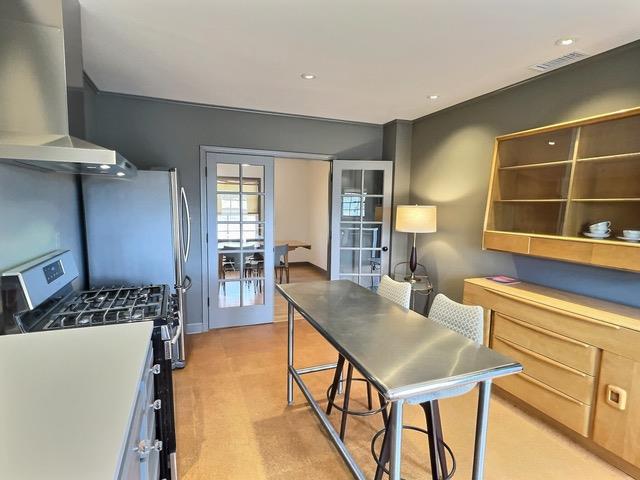 kitchen featuring gas stove, french doors, wall chimney range hood, and light brown cabinets