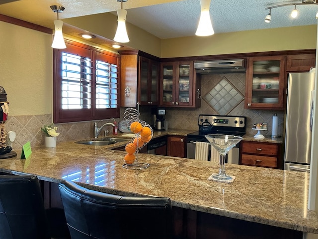 kitchen with a sink, under cabinet range hood, tasteful backsplash, a textured ceiling, and stainless steel appliances