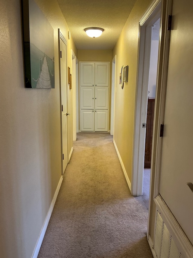 hallway featuring visible vents, light colored carpet, a textured ceiling, and baseboards