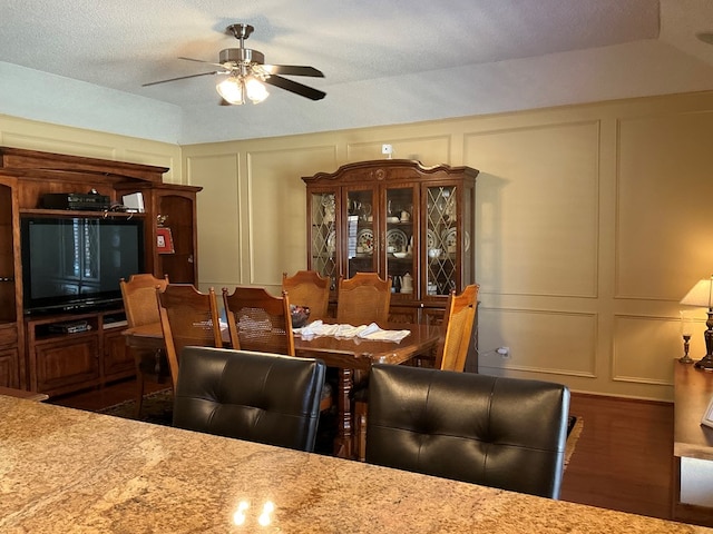 dining room featuring a decorative wall, ceiling fan, and dark wood-style flooring