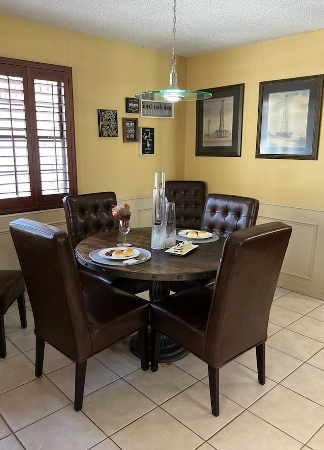 dining space with light tile patterned floors, a wainscoted wall, and a textured ceiling