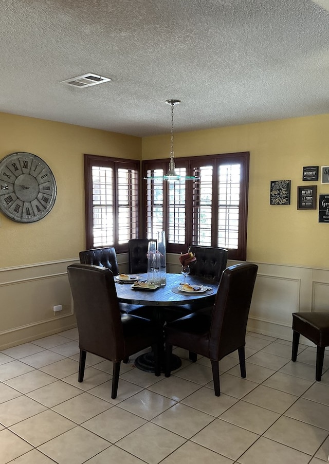 dining space with light tile patterned flooring, visible vents, a healthy amount of sunlight, and a wainscoted wall