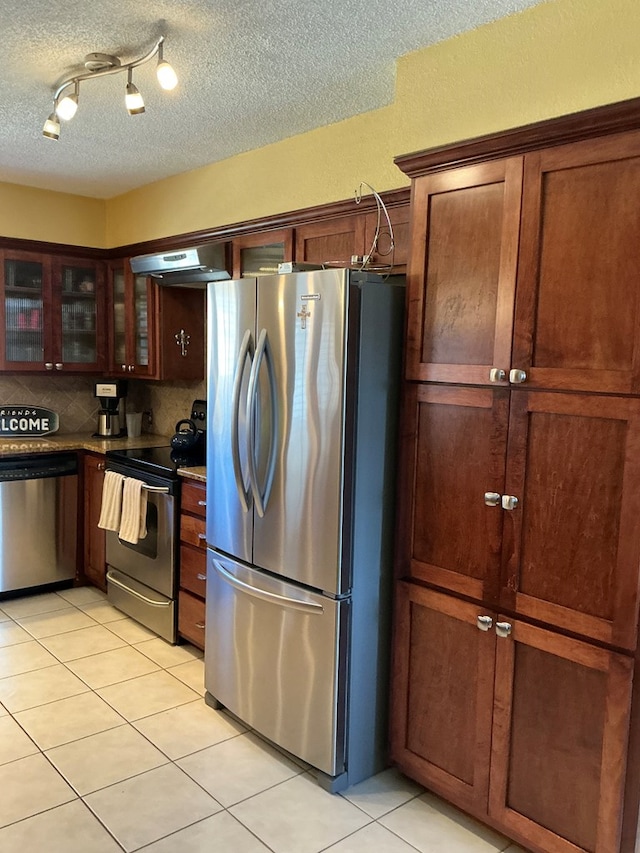 kitchen featuring under cabinet range hood, tasteful backsplash, appliances with stainless steel finishes, light tile patterned floors, and glass insert cabinets