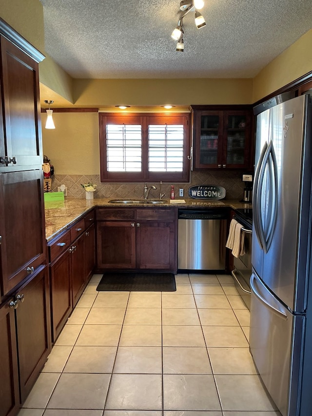 kitchen featuring tasteful backsplash, glass insert cabinets, appliances with stainless steel finishes, light tile patterned flooring, and a sink