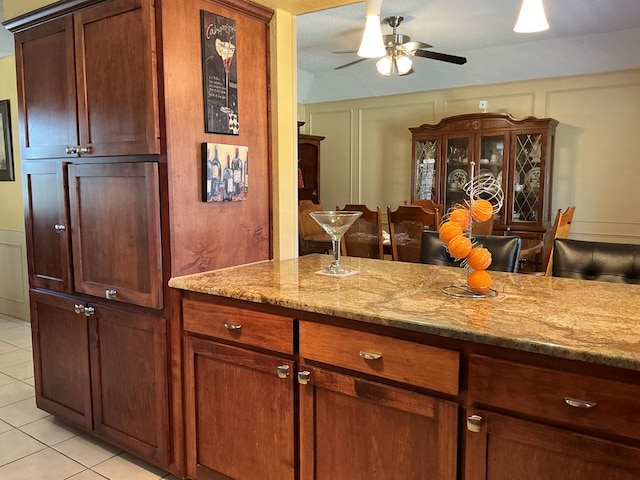 kitchen featuring ceiling fan, light stone countertops, light tile patterned flooring, and a decorative wall