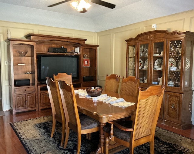 dining area featuring dark wood-type flooring, a decorative wall, and a ceiling fan