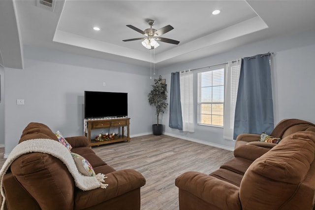 living room featuring a raised ceiling, ceiling fan, and light hardwood / wood-style floors