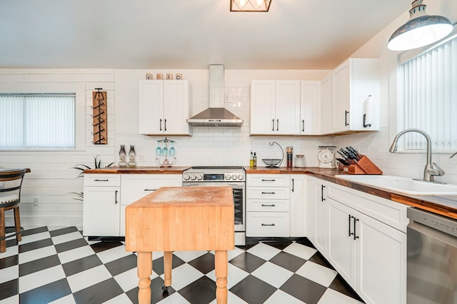 kitchen featuring white cabinets, wall chimney range hood, sink, and appliances with stainless steel finishes