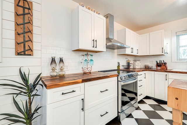 kitchen featuring wooden counters, white cabinets, stainless steel electric range oven, and wall chimney range hood