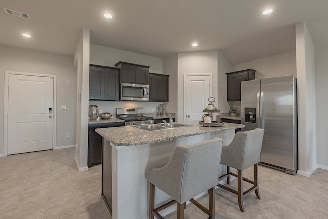 kitchen with light stone counters, a breakfast bar, stainless steel appliances, a kitchen island with sink, and sink