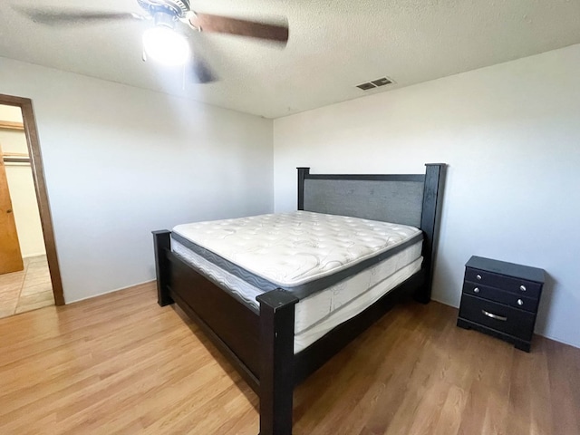 bedroom with visible vents, a textured ceiling, a ceiling fan, and wood finished floors