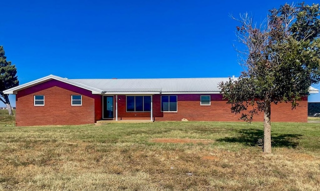 back of house featuring brick siding, metal roof, and a yard