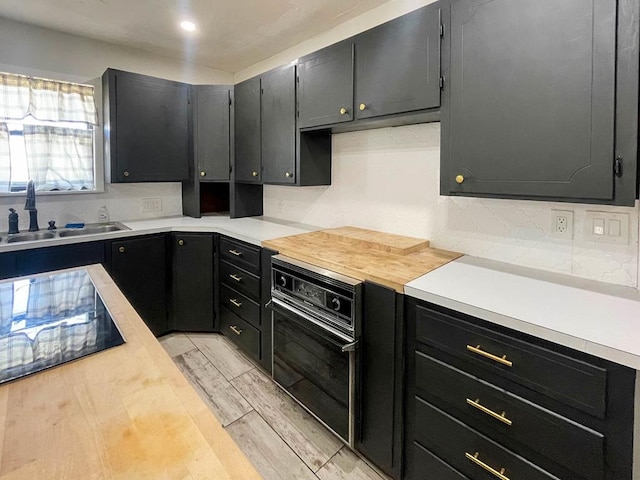 kitchen featuring light wood finished floors, a sink, light countertops, black oven, and tasteful backsplash