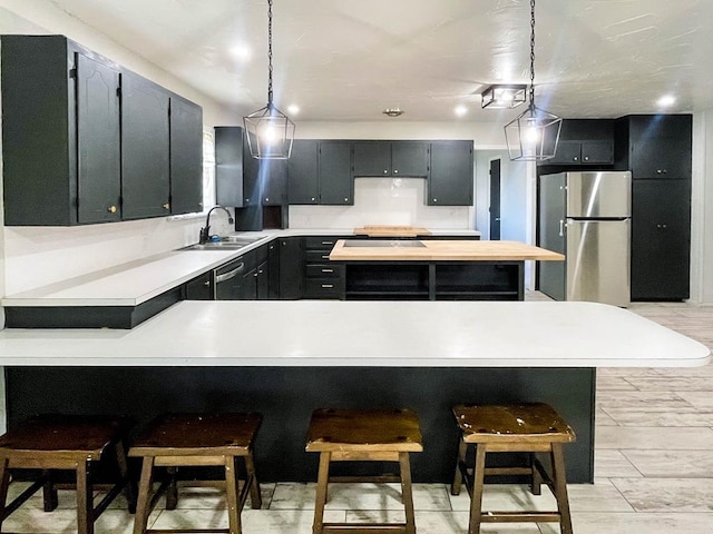 kitchen with a kitchen bar, a sink, stainless steel appliances, a peninsula, and light countertops