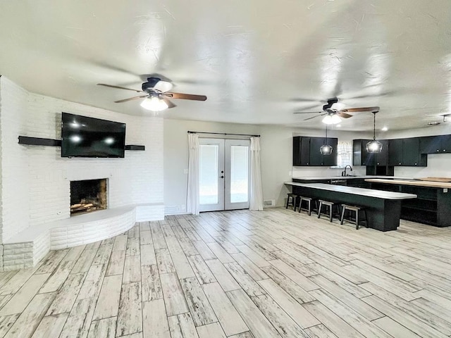 unfurnished living room featuring ceiling fan, light wood-type flooring, french doors, a fireplace, and a sink