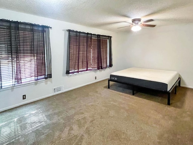 unfurnished bedroom with visible vents, ceiling fan, baseboards, carpet floors, and a textured ceiling