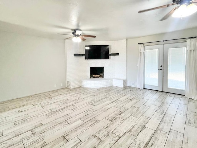 unfurnished living room with light wood-type flooring, a brick fireplace, a ceiling fan, and french doors