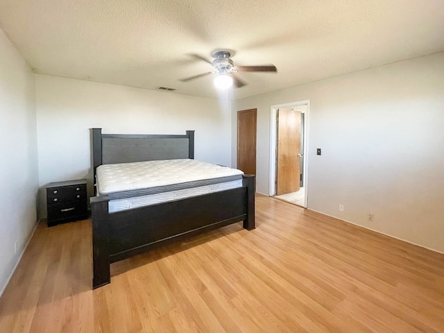 bedroom featuring ceiling fan, visible vents, a textured ceiling, and light wood-style flooring