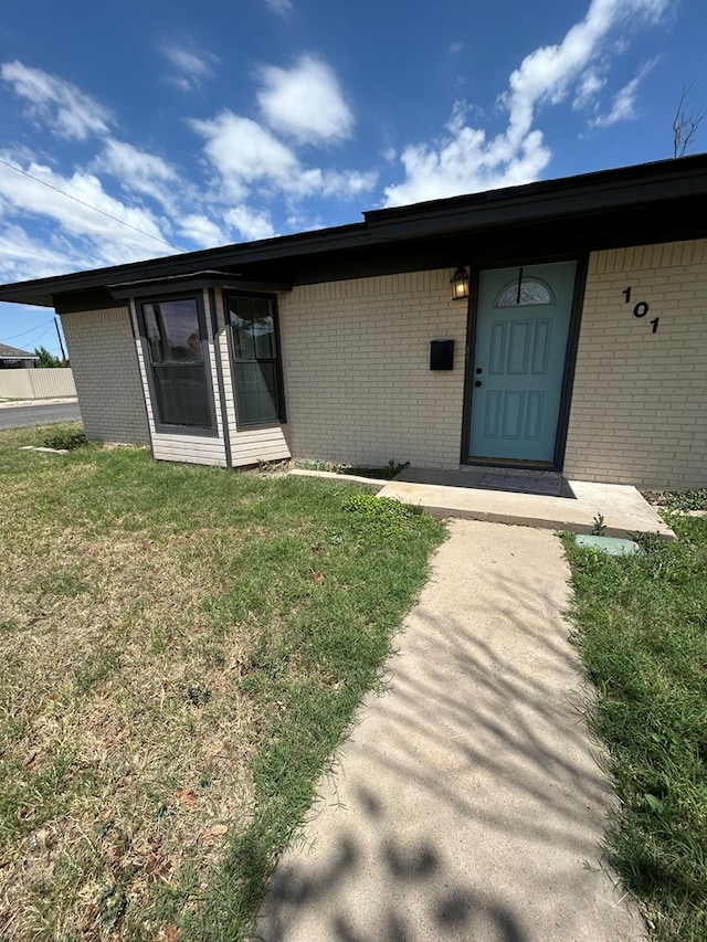 view of exterior entry featuring a lawn and brick siding