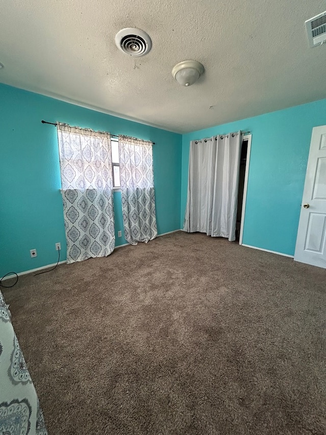 carpeted spare room featuring a textured ceiling and visible vents