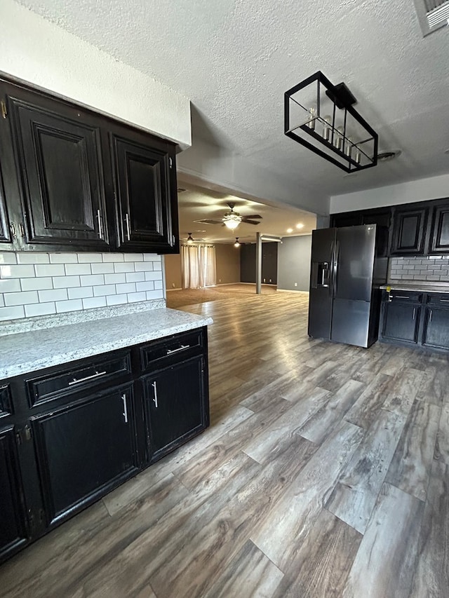 kitchen featuring black fridge, light wood finished floors, light countertops, dark cabinets, and decorative backsplash