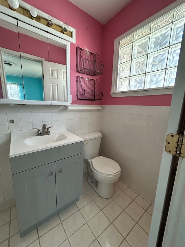 half bathroom featuring vanity, toilet, tile patterned floors, a wainscoted wall, and tile walls