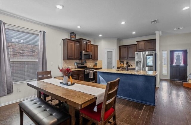 7012 Perot Ranch Rd, Odessa, TX 79765 - kitchen featuring appliances with stainless steel finishes, a sink, ornamental molding, dark brown cabinets, and a center island with sink