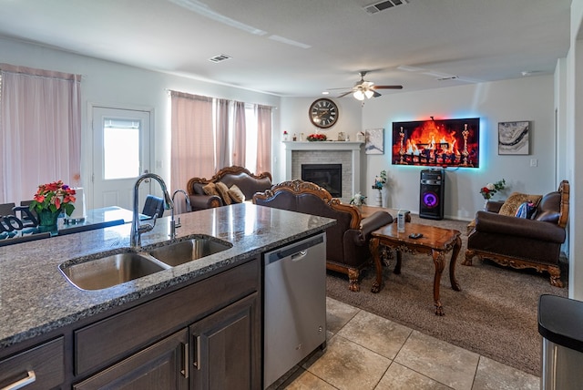 kitchen featuring sink, dishwasher, dark stone countertops, dark brown cabinets, and a brick fireplace