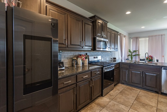 kitchen with backsplash, appliances with stainless steel finishes, sink, and dark stone countertops