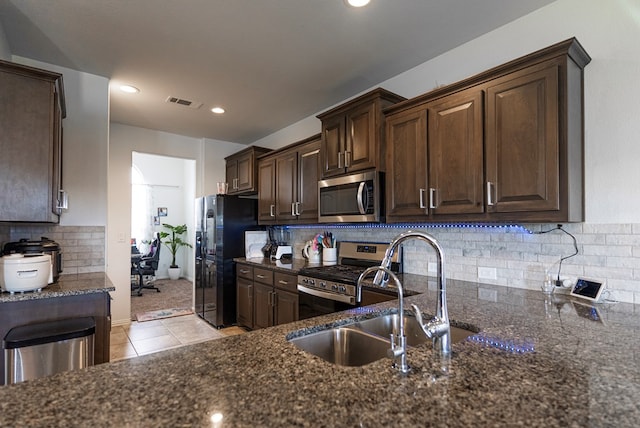 kitchen with sink, dark brown cabinets, dark stone counters, stainless steel appliances, and backsplash