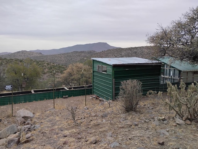 view of outdoor structure with fence, a mountain view, and an outbuilding